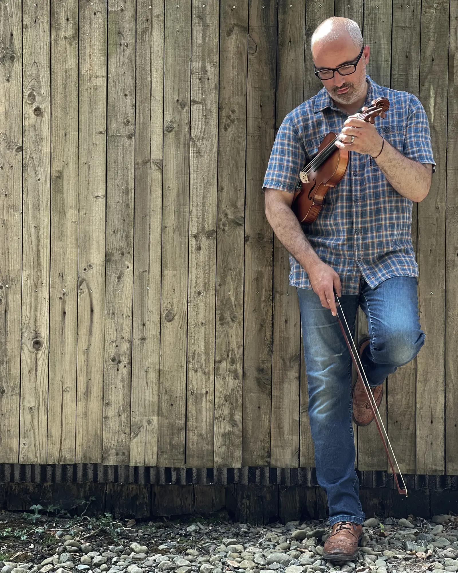 Dave Mackay leaning against a weathered fence with his fiddle